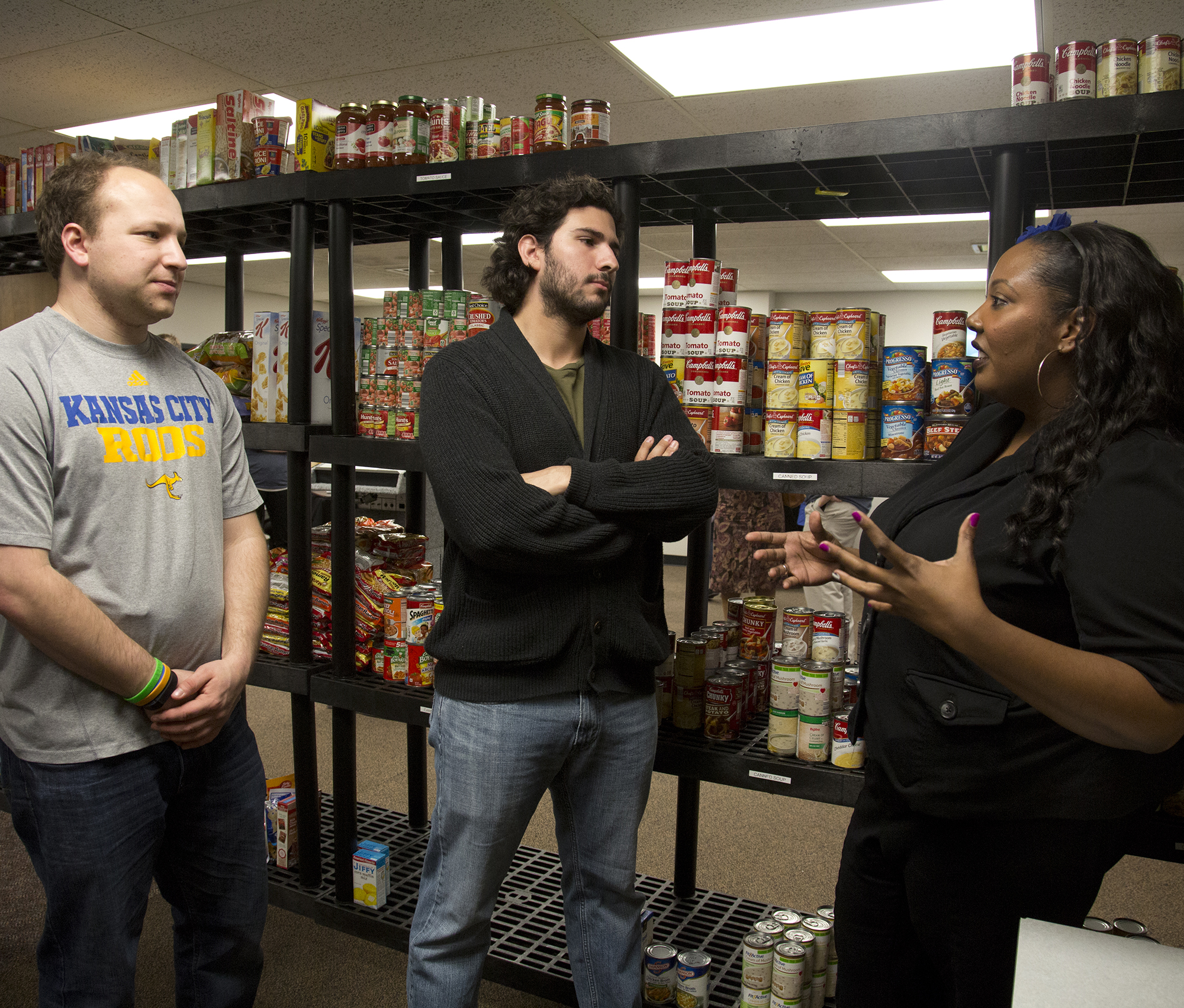 three people stand in front of shelves filled with canned goods in the Kangaroo Pantry